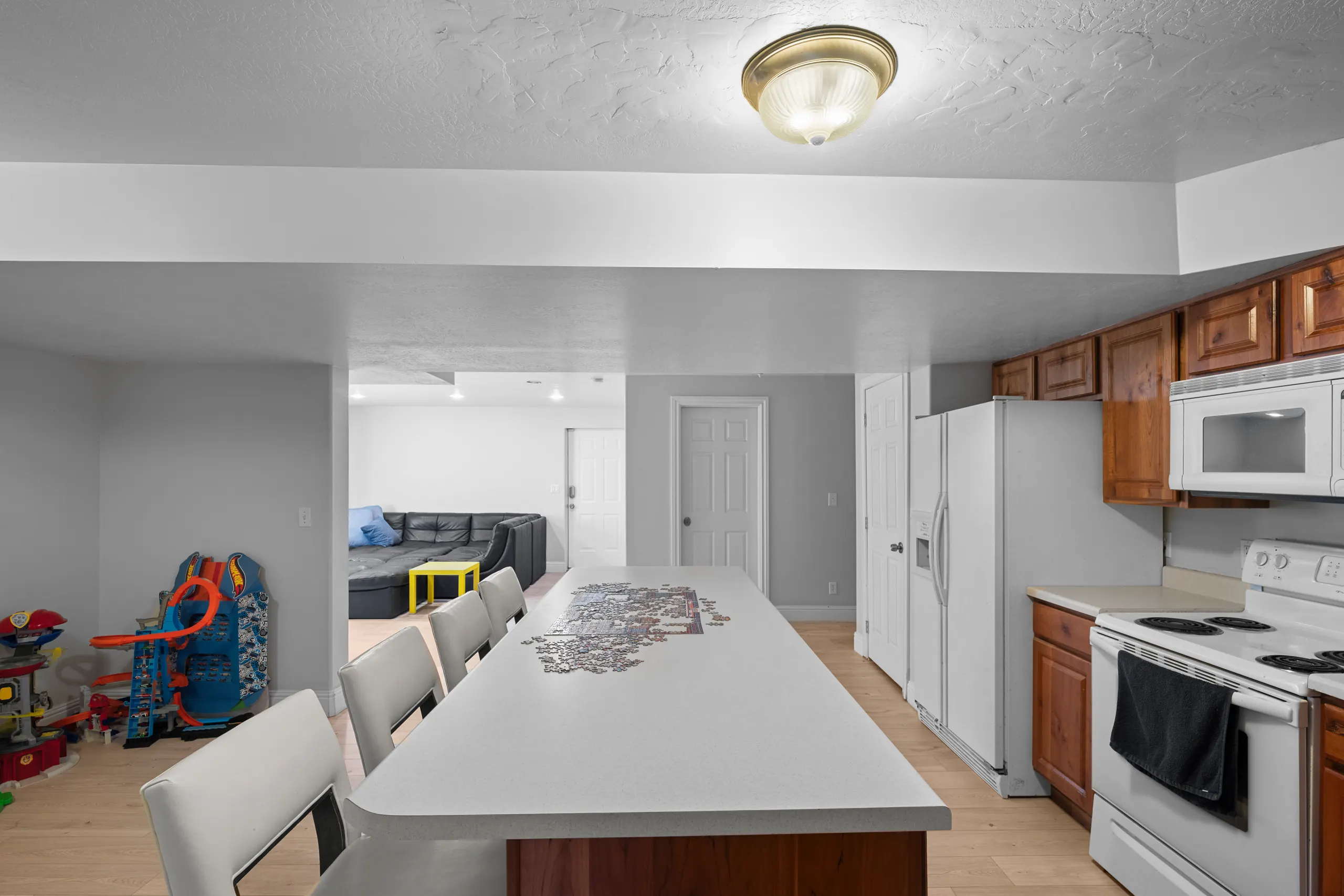 Basement family room seen past a long quartz island with bar seating, opening to a sectional and play area