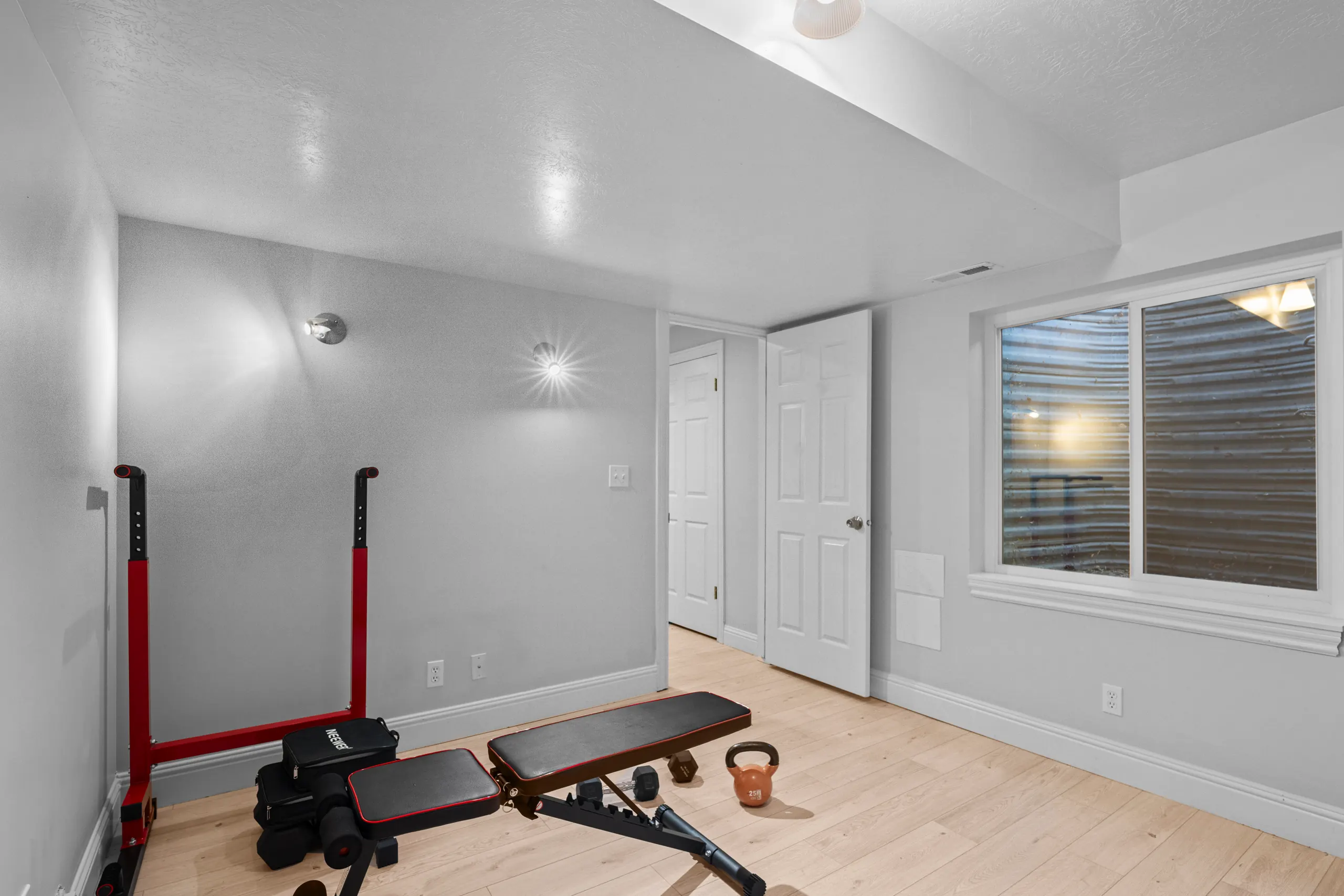 Basement home gym with a weight bench, squat stand and kettlebell beside a daylight window well