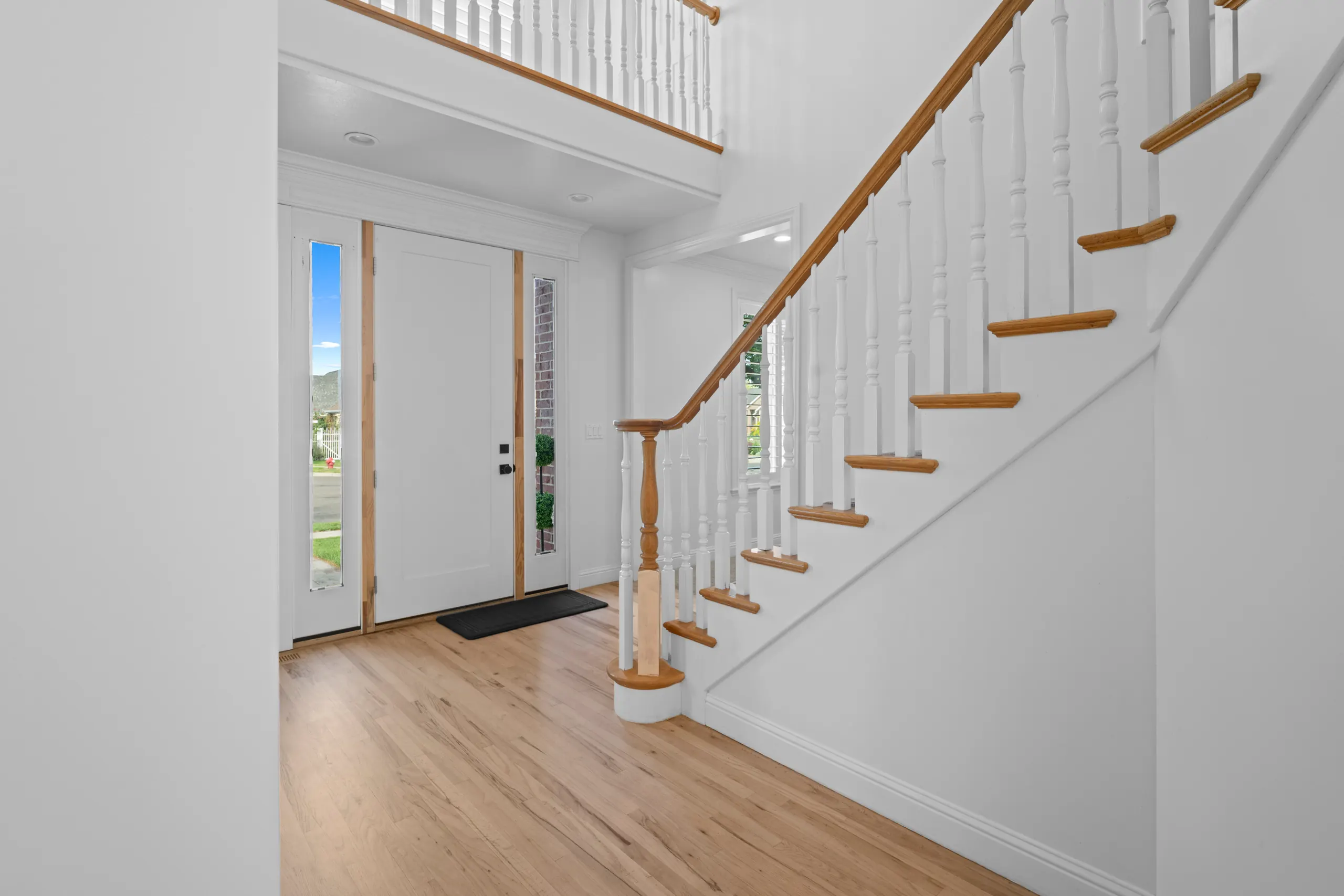 Two-story entryway with an open staircase, oak treads and handrail, white balusters and light oak floors running in from the front door